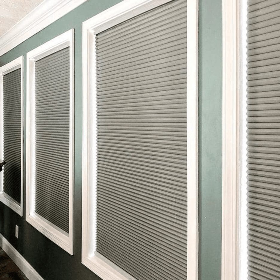 four windows pictured with gray cellular blinds within a white border on a light green wall.