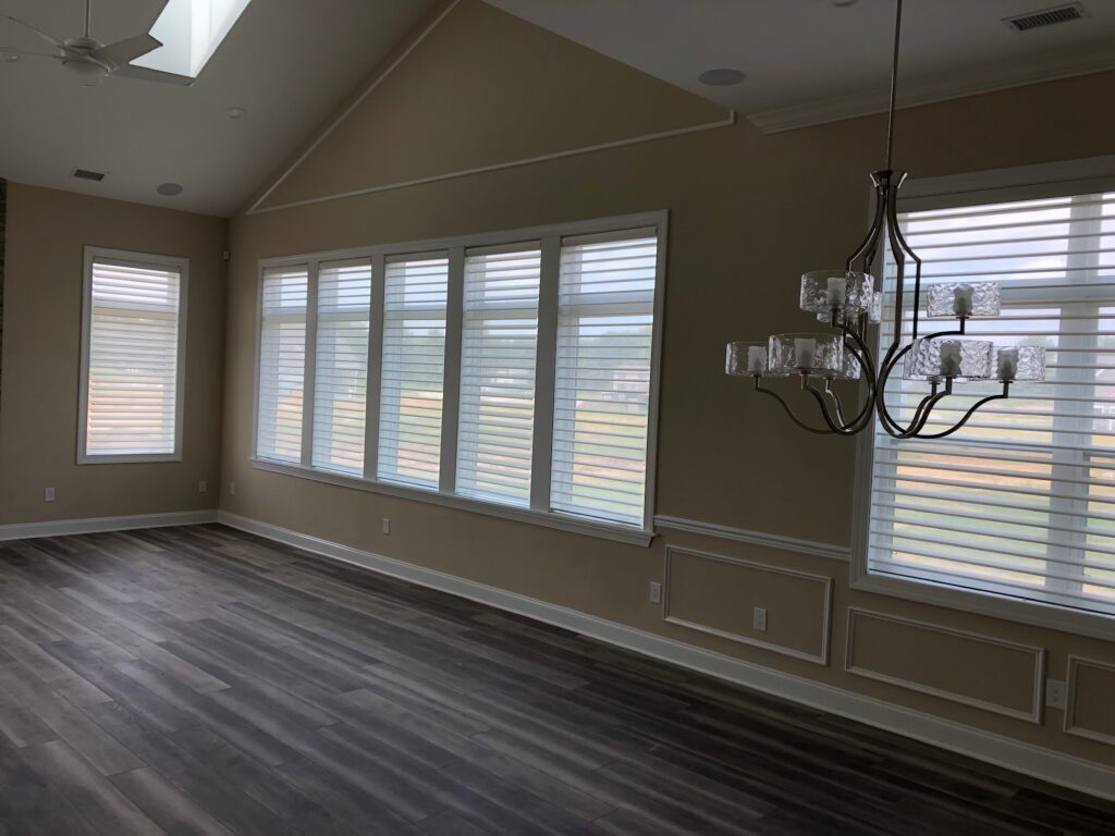 Six tall slender windows covered by motorized blinds near a large window in an open room with vaulted ceilings.