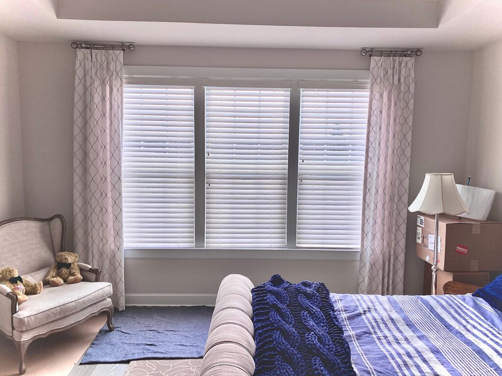 Bedroom with composite blinds, a chair in the corner with 2 teddy bears, and a lamp.