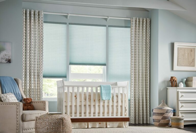 Three adjacent windows with cellular shades in back of custom drapes, framing a baby crib in a children's bedroom.