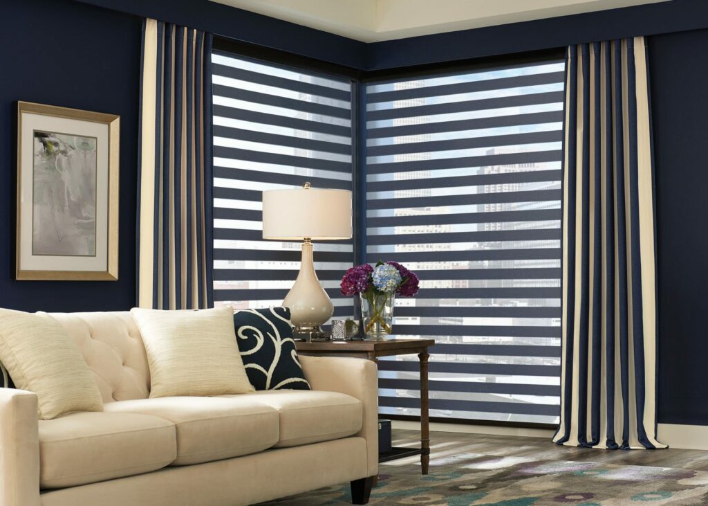 Bartlett Blind’s versatile and durable custom drapes hanging on both sides of a corner window and pooling on the floor in a living room.
