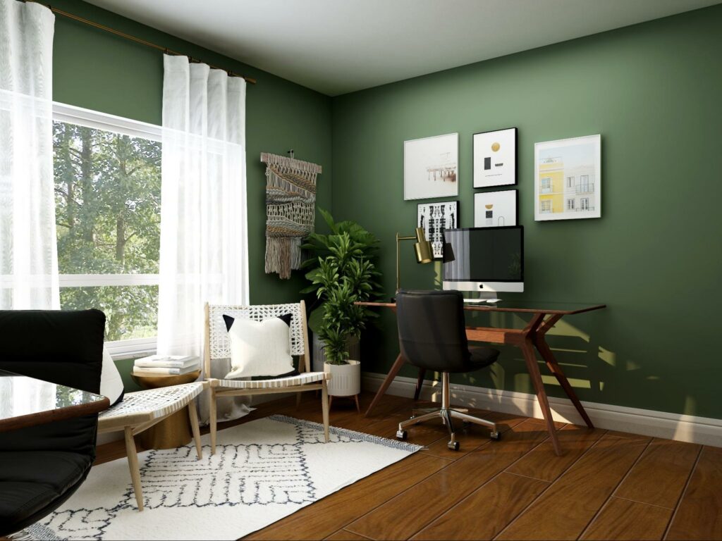 Furnished home office with green walls, hardwood flooring, and long white curtains.