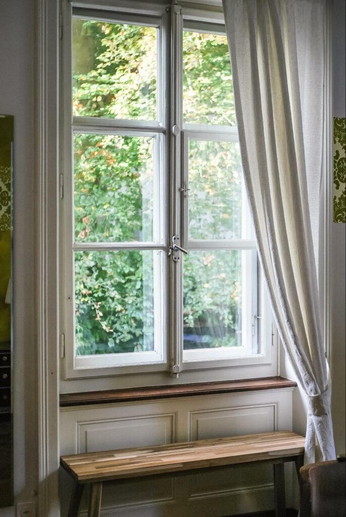 White curtains pulled to the side with windows facing trees.