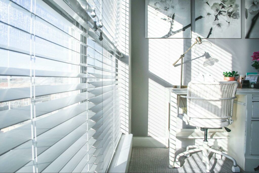 White window blinds next to a white office desk and chair during the daytime.