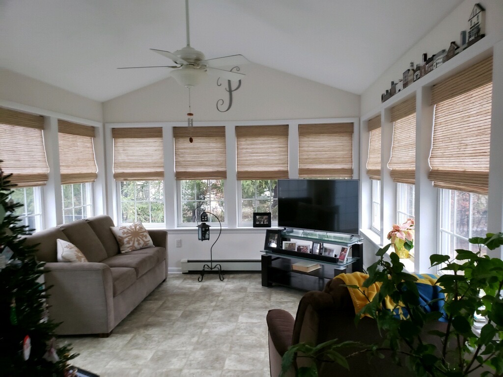 A rec room with a couch, recliner, and TV surrounded by multiple windows with custom shades.