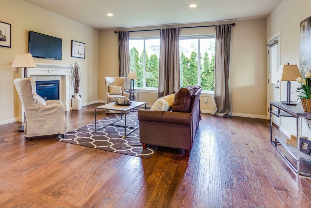 Furnished living room with hardwood floors, two large windows with floor-length curtains.